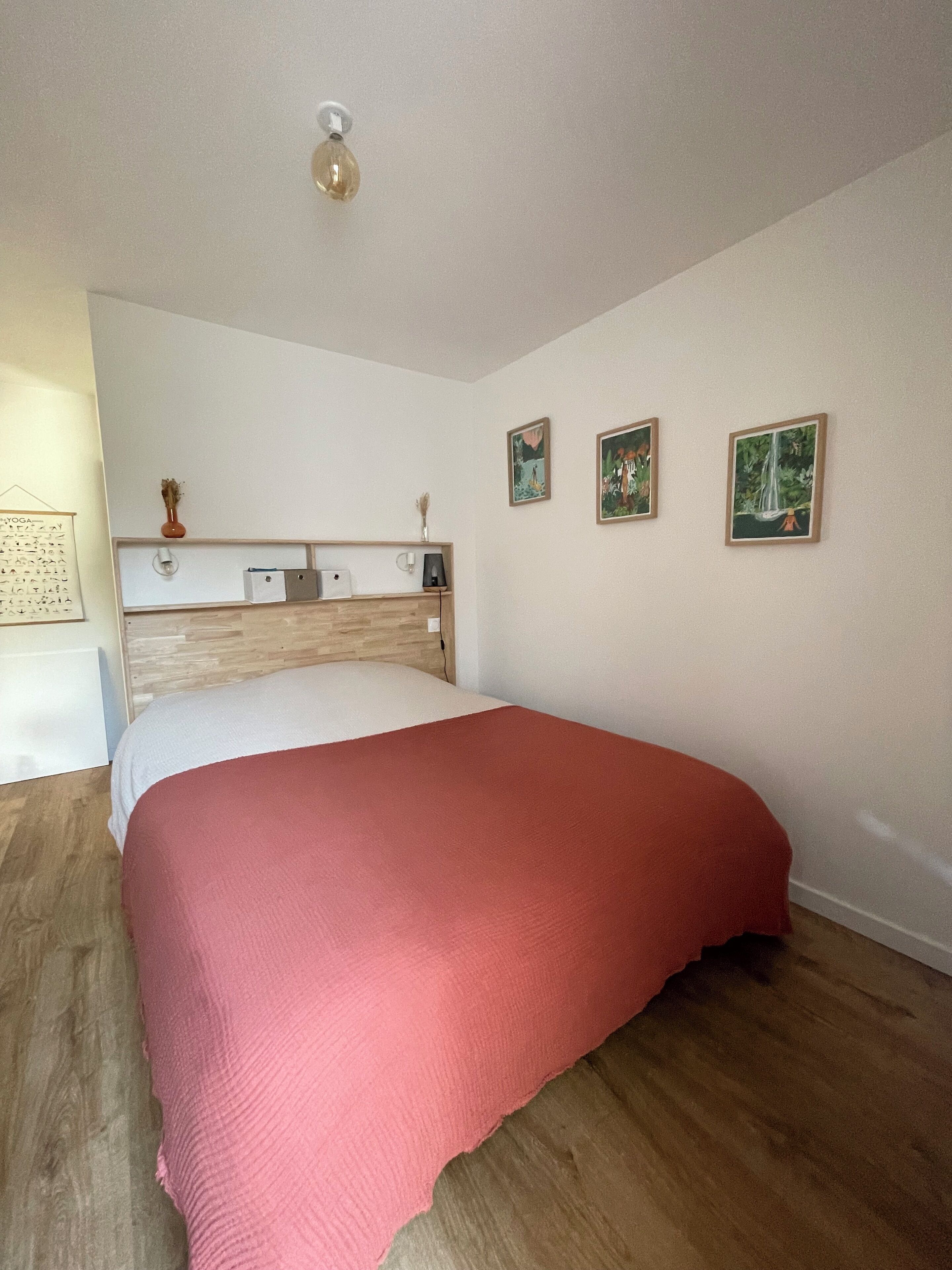Une chambre à coucher avec une tête de lit en bois, un lit recouvert d’une couverture rose et trois tableaux encadrés accrochés au mur.