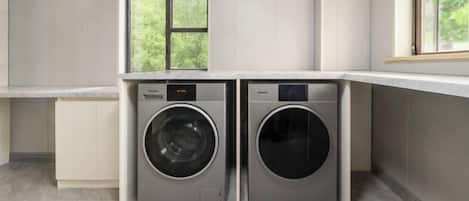 A laundry room with two front-loading washing machines, a window above them, and a countertop.