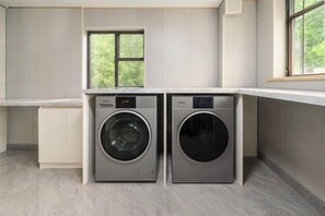 A laundry room with two front-loading washing machines, a window above them, and a countertop. - Huayi Hotel (Shanghai)