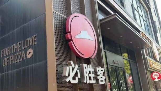 A storefront with a pizza restaurant sign and a red circular logo. - Huayi Hotel (Shanghai)
