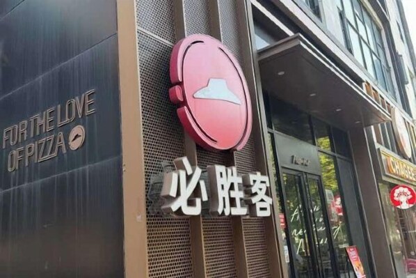 A storefront with a pizza restaurant sign and a red circular logo. - Huayi Hotel (Shanghai)