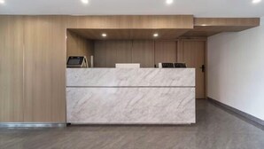 Un espace d’accueil avec un comptoir en marbre, des murs recouverts de panneaux en bois et une porte visible au fond.