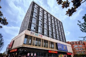 A multi-story building with a modern architectural design, featuring a prominent glass facade and a ground-level commercial space with signage. - Huayi Hotel (Shanghai)