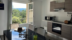Une cuisine moderne avec vue sur la verdure et un balcon, comprenant une table à manger avec des chaises, un four à micro-ondes et une machine à café.