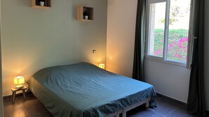 Une chambre à coucher avec un lit, des lampes de chevet, une fenêtre avec des rideaux et deux étagères murales ornées de plantes.