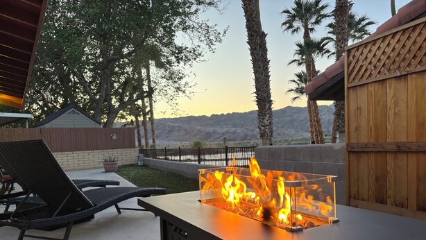 Eine Außenpatio mit einem Metall-Feuertisch, Lounge-Stühlen und einem Holzzaun.