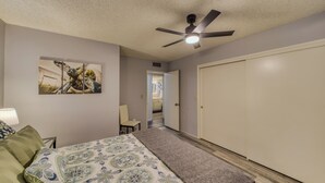Ein Schlafzimmer mit einem Bett, einem Deckenventilator, einer Tür und einem Flur, der in ein weiteres Zimmer führt.