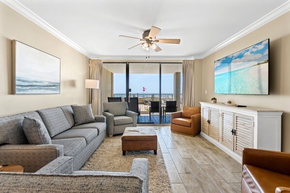 A living room with a sofa, armchairs, a TV, a ceiling fan, and a view through a glass door to the outside.