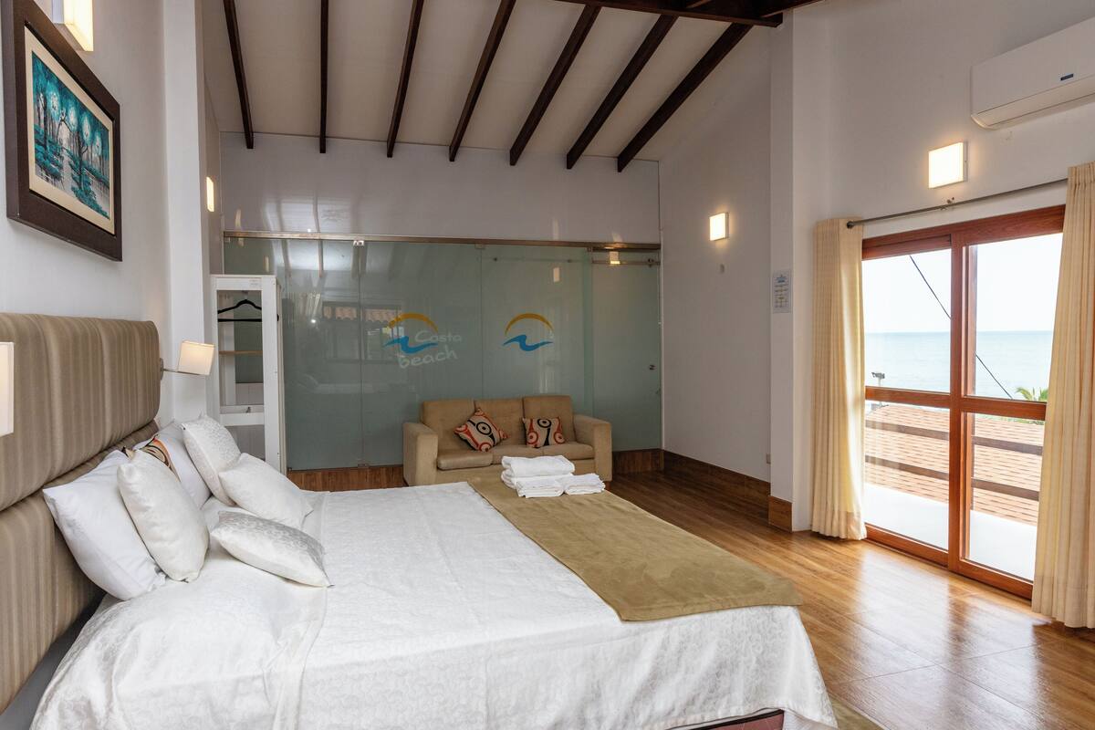 Hotelkamer met een bed, een slaapbank, een glazen wand met een logo en uitzicht op zee.