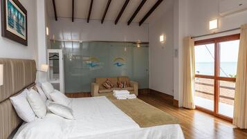 Habitación de hotel con cama, sofá, pared de vidrio con un logotipo y vista al mar.