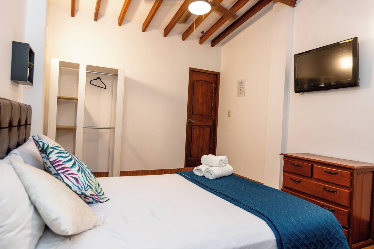 Een slaapkamer met een bed, een kledingkast, een televisie en een houten plafond.