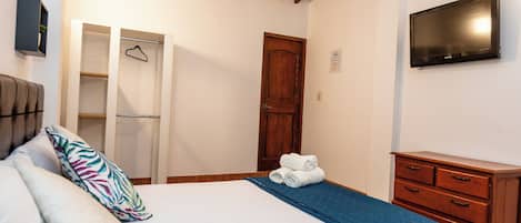 Un dormitorio con cama, armario, televisor y techo de madera.