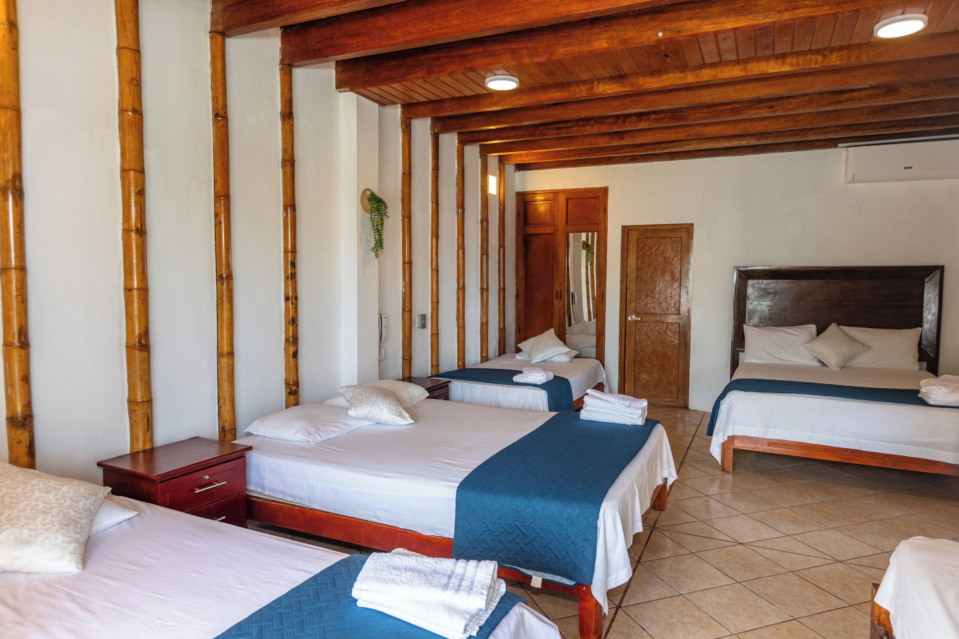A hotel room with four beds, wooden headboards, and a tiled floor.