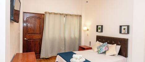 A bedroom with a wooden door, a bed with a blue blanket, a bedside table, and a nightstand with a lamp.