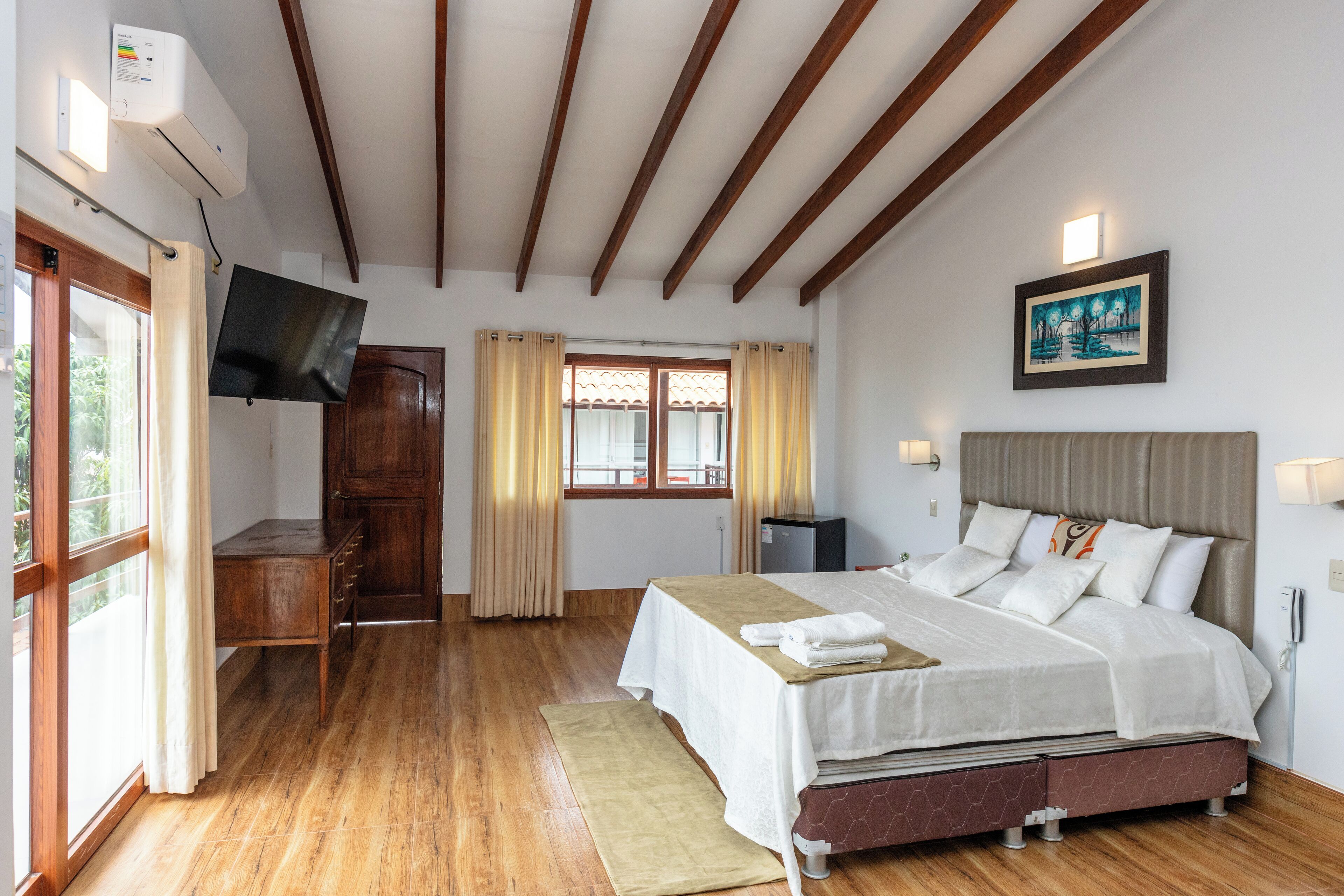 A hotel room with a bed, bedside table, TV, and a painting on the wall.