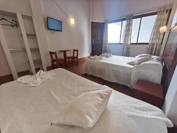 Habitación de hotel con dos camas, un escritorio, una silla y un armario.