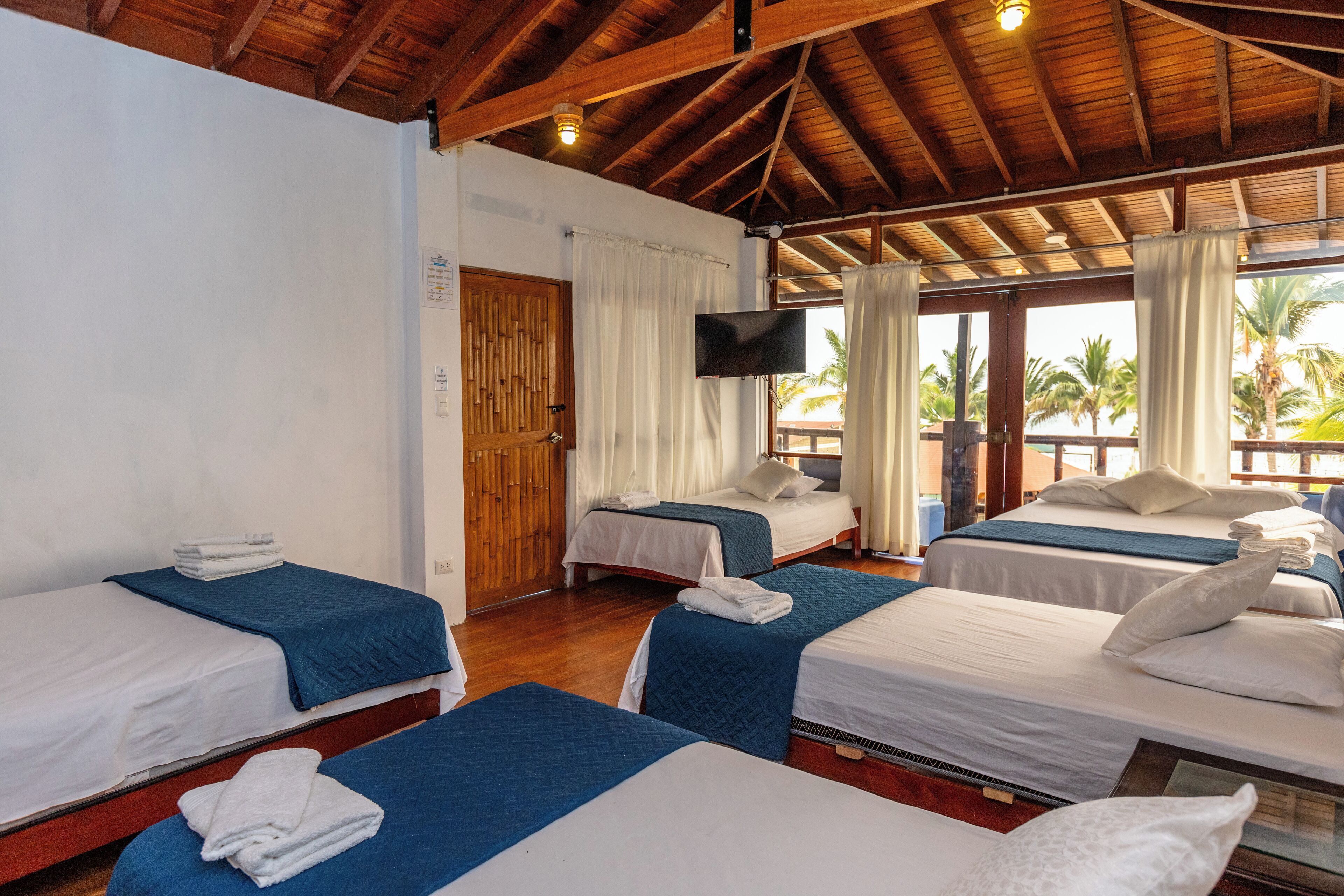 A hotel room with three single beds, a TV, and a wooden ceiling.