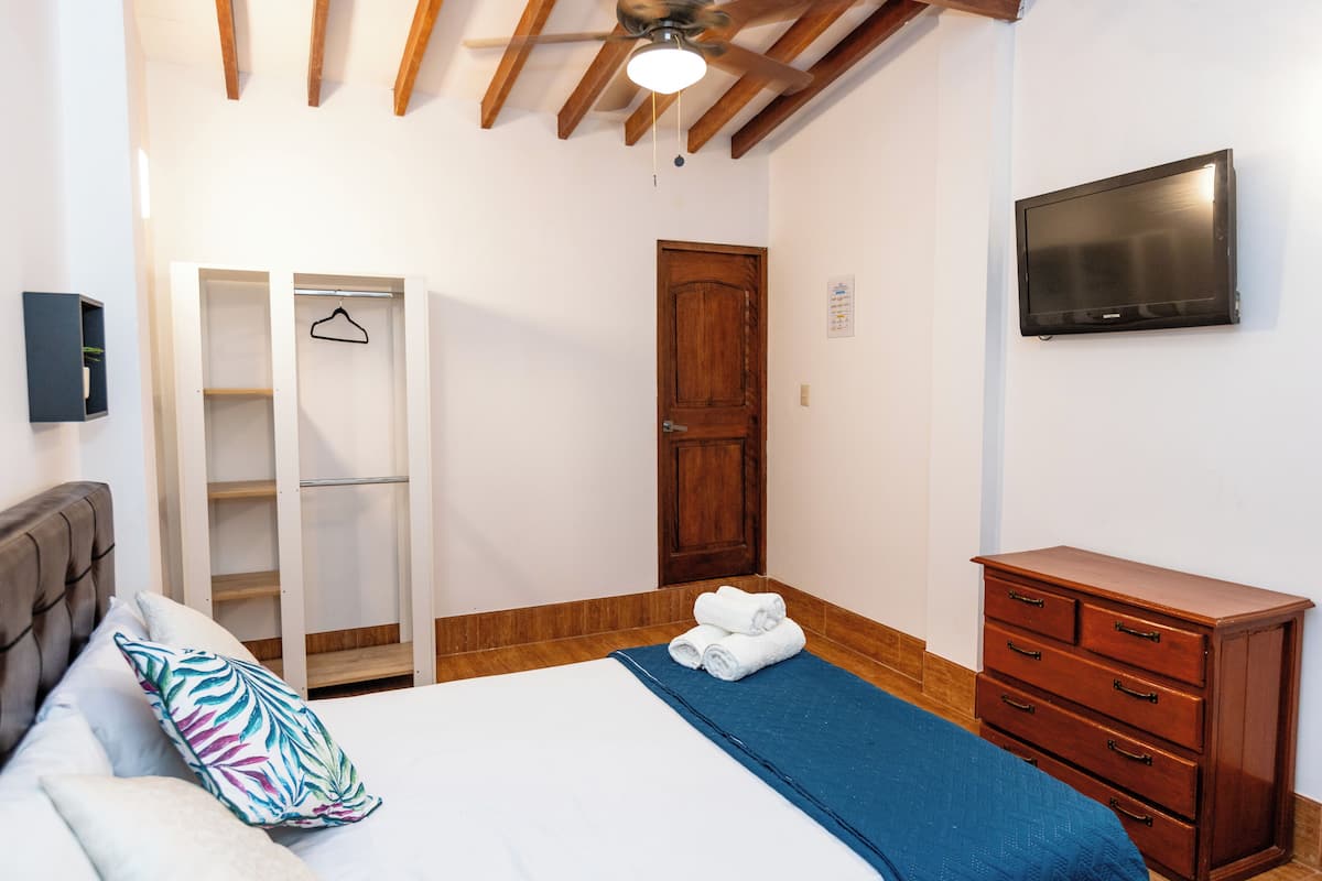 Een slaapkamer met een bed, een kledingkast, een dressoir, een televisie en een plafondventilator.
