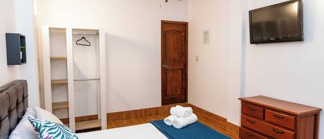 Un dormitorio con cama, armario, tocador, televisor y ventilador de techo.