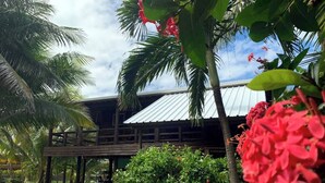 A wooden structure with a metal roof, surrounded by lush greenery and palm trees.