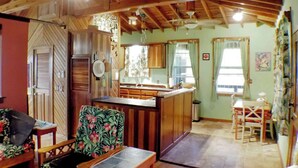 A cozy cabin interior with a wooden ceiling, a dining area, and a kitchen.