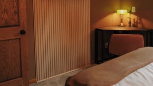 Une chambre d’hôtel avec un lit, un bureau doté d’une lampe, un téléviseur fixé au mur et un ventilateur de plafond.
