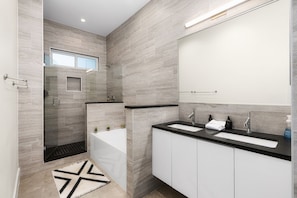 Une salle de bain moderne avec deux lavabos, une douche à l’italienne en verre et un grand miroir.