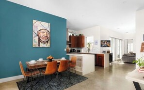 Een moderne keuken met houten kastjes, een centraal eiland en een eethoek met een blauwgroene accentmuur en een schilderij.
