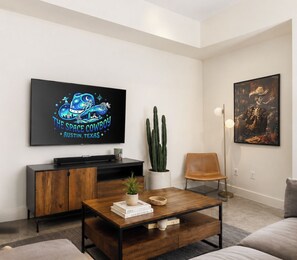 Een moderne woonkamer met een flatscreen televisie, een houten salontafel, een cactusplant, een boekenkast en een kunstwerk in een lijst aan de muur.