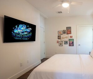 A bedroom with a large bed, a flat-screen TV mounted on the wall, and a door with a framed picture.