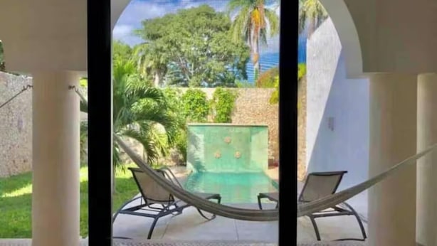 A view through an arched window of a pool area with two lounge chairs and a green pool. - Luxury Home & Pool, 5 Min from Downtown (Merida)