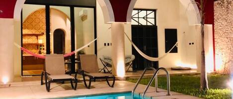 A pool area with lounge chairs and a red building with arched doorways.