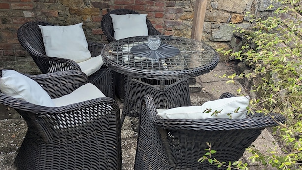 Wicker furniture with cushions, a glass table, and a stone wall with a brick fireplace. - Bright, cozy vacation apartment for 3-4 people (Kalletal)