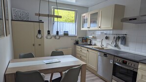A modern kitchen with a wooden dining table, two chairs, a built-in oven, and a dishwasher. - Bright, cozy vacation apartment for 3-4 people (Kalletal)