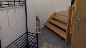 A room with a black metal coat rack, a macrame wall hanging, a wooden door, and a small white lantern on the floor. - Bright, cozy vacation apartment for 3-4 people (Kalletal)