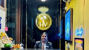 A hotel reception desk with a chandelier, a logo, and a TV screen. - HolidayVilla & Suites Amritsar (Amritsar)