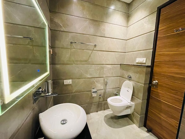 Et moderne badeværelse med toilet, bidet og et stort spejl.