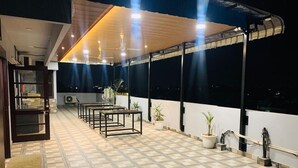 A covered outdoor area with a tiled floor, a table and chairs, potted plants, and a railing. - HolidayVilla & Suites Amritsar (Amritsar)