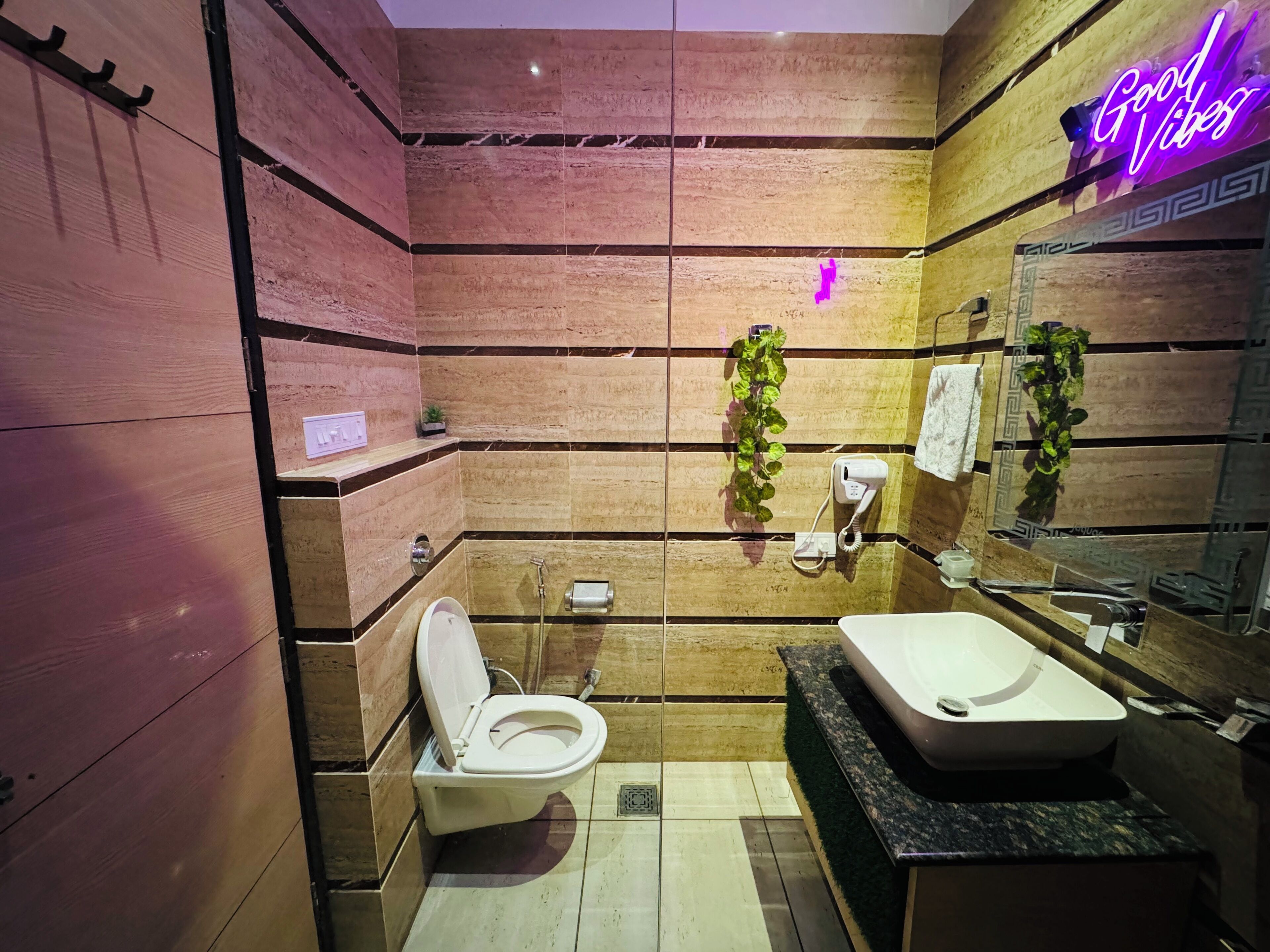 Un baño moderno con diseño de pared de madera, un inodoro blanco, un lavamanos grande y un letrero de neón que dice 'Good Vibes'.