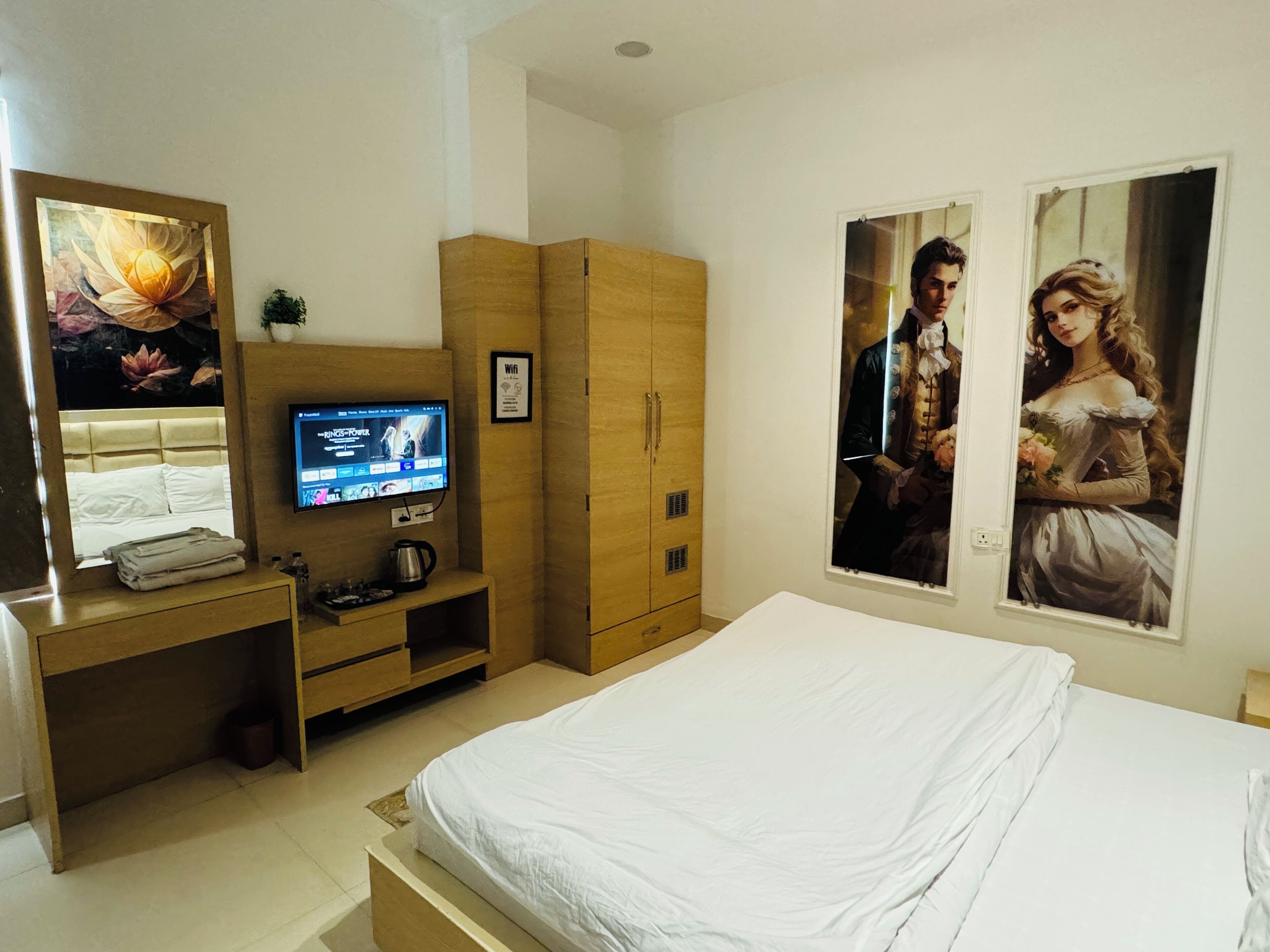A bedroom with a bed, a TV, wooden wardrobe, and two framed pictures on the wall.