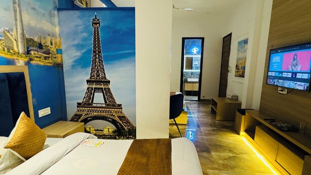 A hotel room with a large mural of the Eiffel Tower, a bed with white linens, a wooden headboard, and a television on the wall. - HolidayVilla & Suites Amritsar (Amritsar)