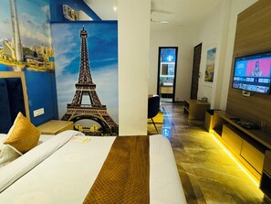 A hotel room with a large mural of the Eiffel Tower, a bed with white linens, a wooden headboard, and a television on the wall. - HolidayVilla & Suites Amritsar (Amritsar)