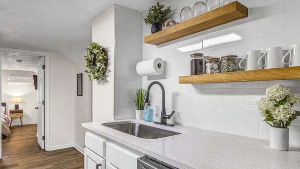 A modern kitchen with white cabinetry, a stainless steel sink, and wooden shelves above.