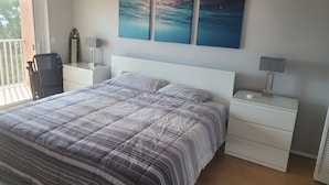A bedroom with a bed, nightstands, a desk, a chair, and artwork on the wall.