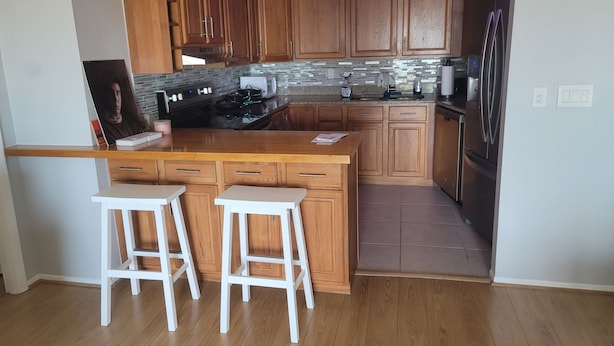 A modern kitchen with wooden cabinets, a stainless steel refrigerator, and a built-in island with bar stools.