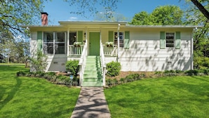 A single-story house with a green front door, a front porch with steps, and a chimney. - Outdoor Grill & Games Near Downtown Shops & Dining (Locust Grove)