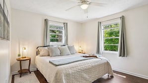 A bedroom with a bed, two bedside tables, a ceiling fan, and two windows with curtains. - Outdoor Grill & Games Near Downtown Shops & Dining (Locust Grove)