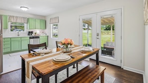 A dining area with a wooden table set for four, green cabinets, and a view of the backyard through a sliding glass door. - Outdoor Grill & Games Near Downtown Shops & Dining (Locust Grove)