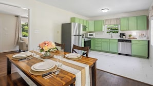 A modern kitchen with green cabinets, stainless steel appliances, and a dining area with a wooden table set for four. - Outdoor Grill & Games Near Downtown Shops & Dining (Locust Grove)