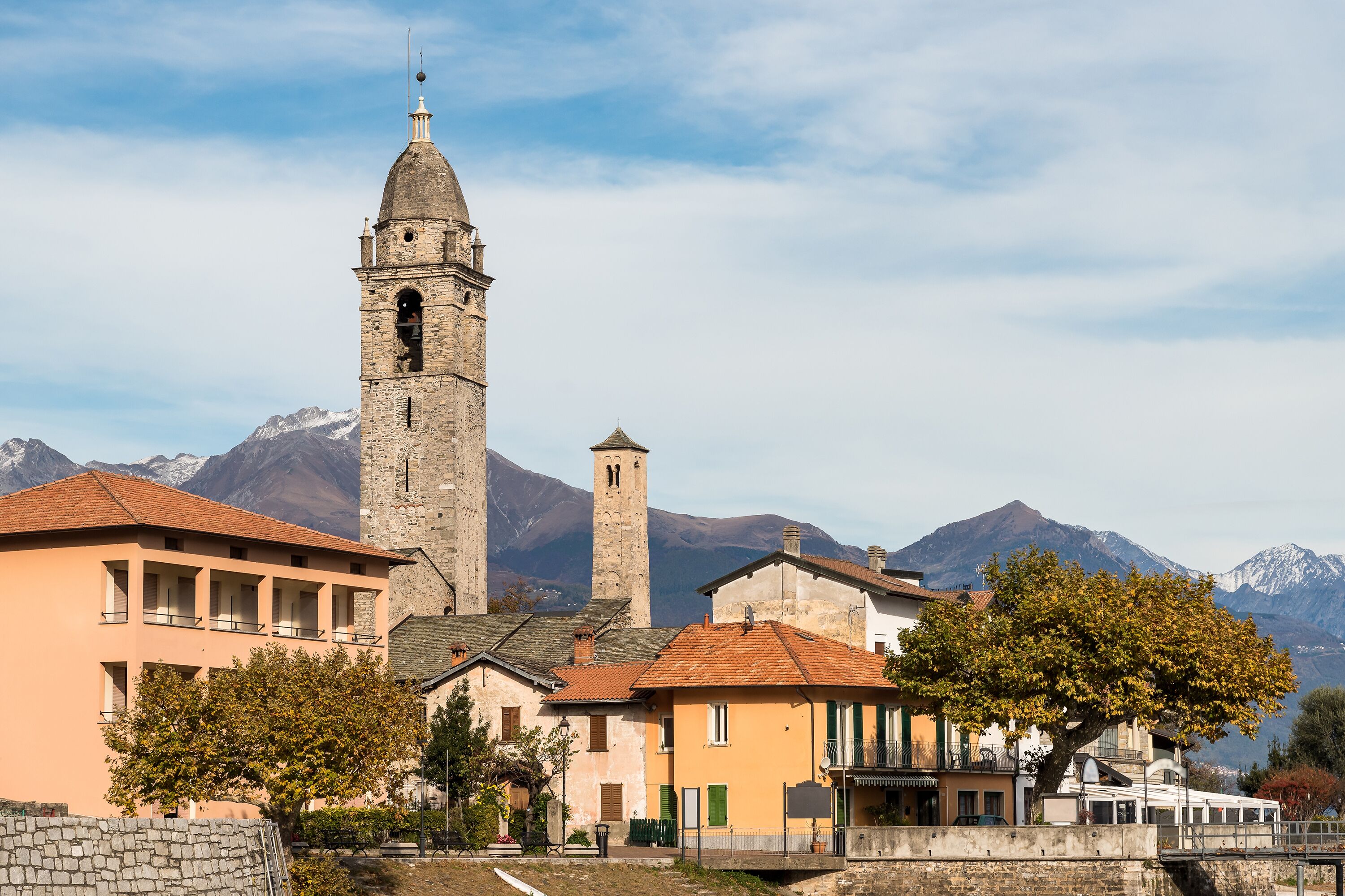 Un edificio histórico con un campanario, rodeado de viviendas y montañas al fondo.